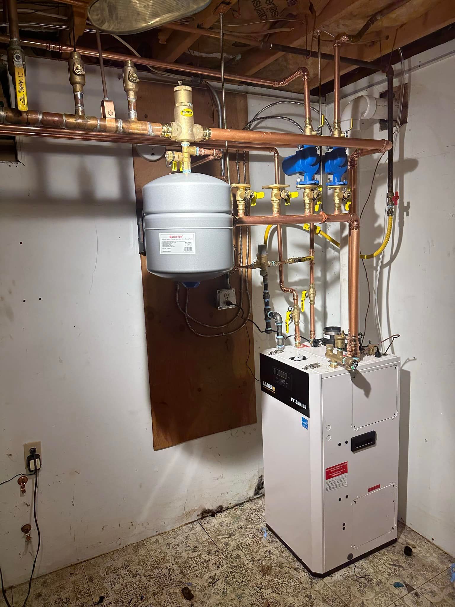 A boiler is sitting in a basement next to a copper pipe.