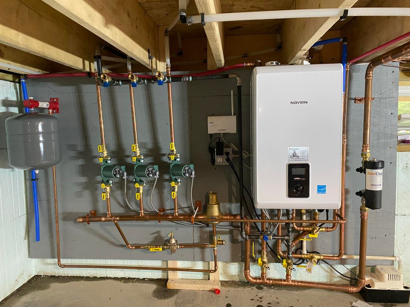 A water heater is installed in a basement with copper pipes.
