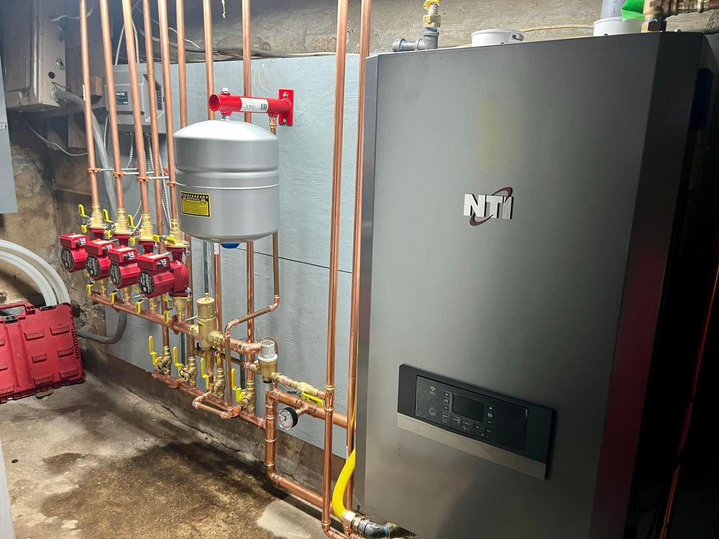 A boiler is being installed in a basement with copper pipes.