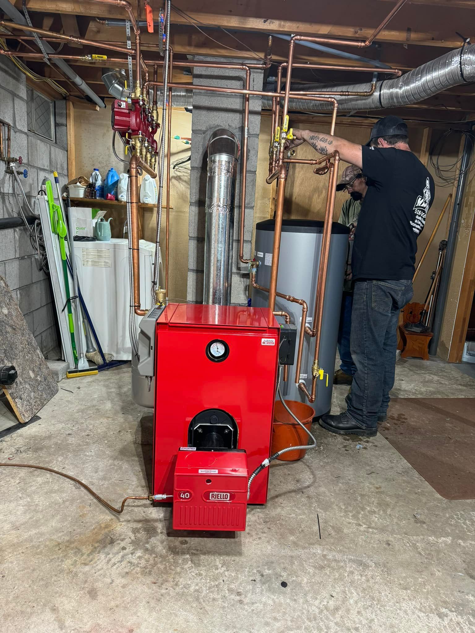 A man is working on a red boiler in a basement.