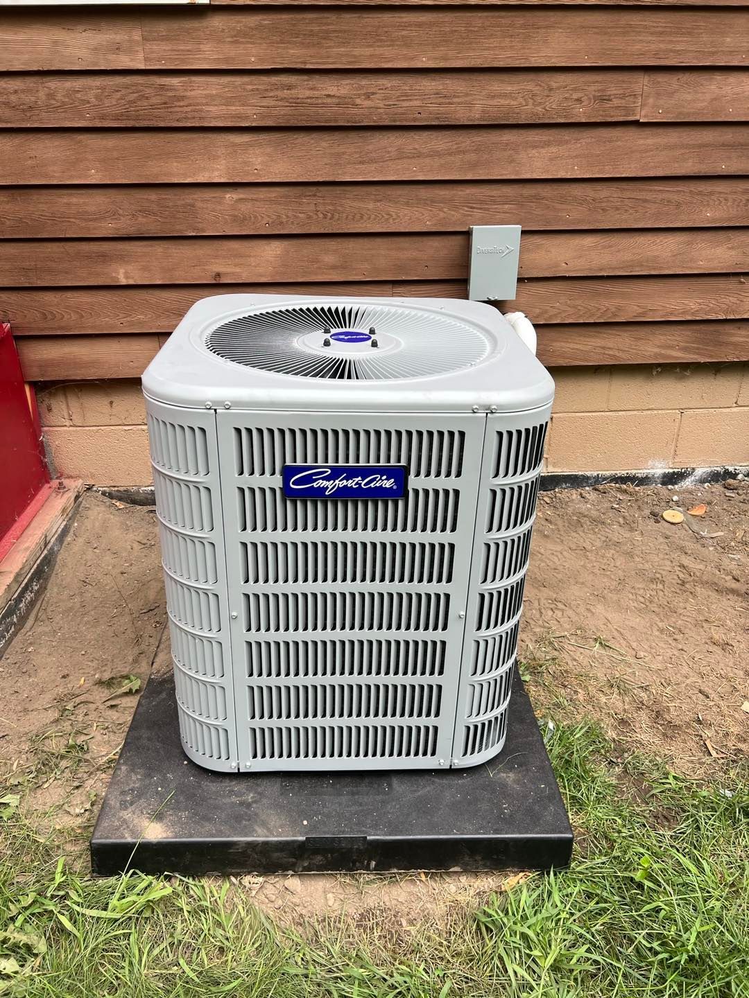 A carrier air conditioner is sitting on top of a black platform in front of a house.