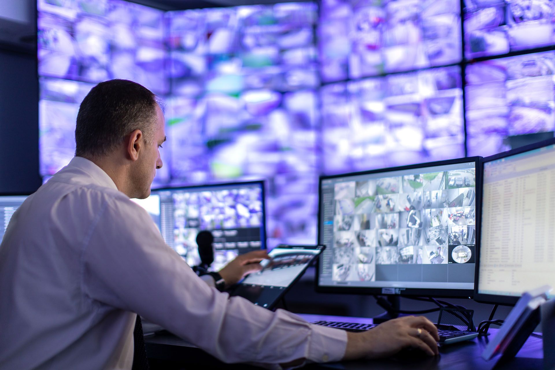 A man is sitting at a desk in front of a bunch of computer monitors