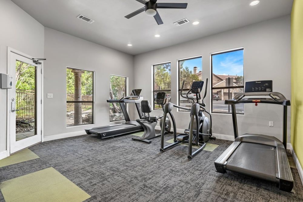 a gym with treadmills, exercise bikes, and a ceiling fan at Marquis at Caprock Canyon in Austin, TX.