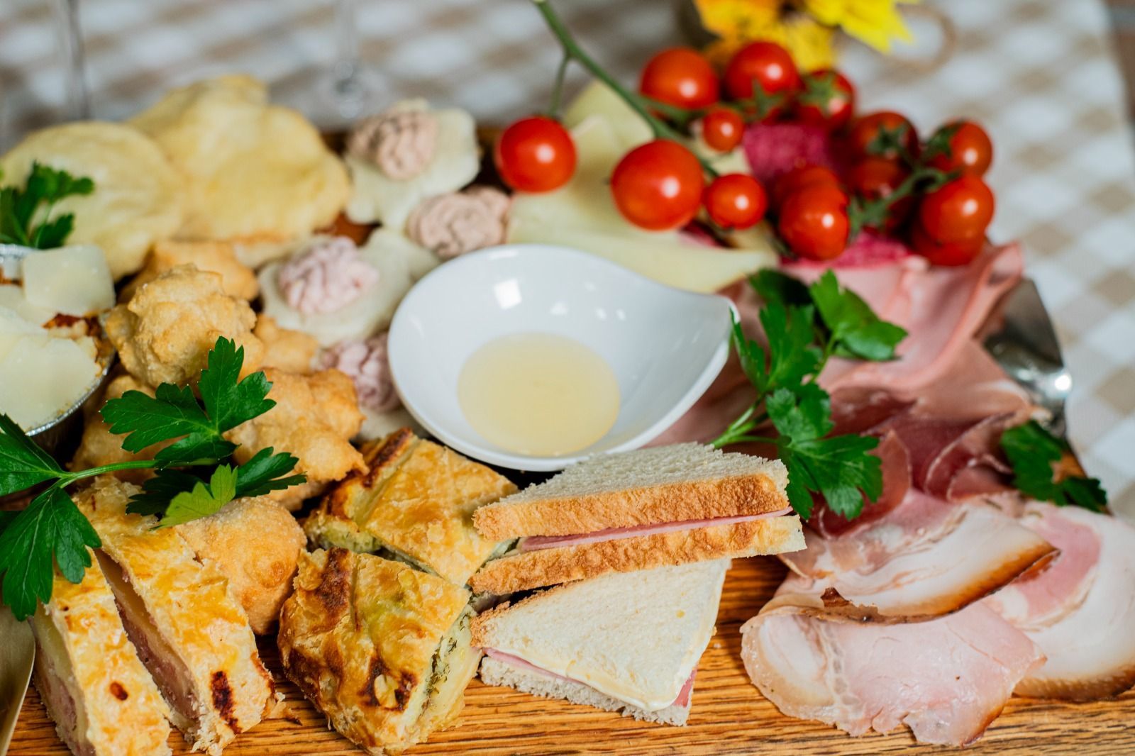 Formaggi assortiti, salumi, pane, pomodori ed erbe aromatiche disposti su un tavolo rustico con una piccola ciotola d'olio