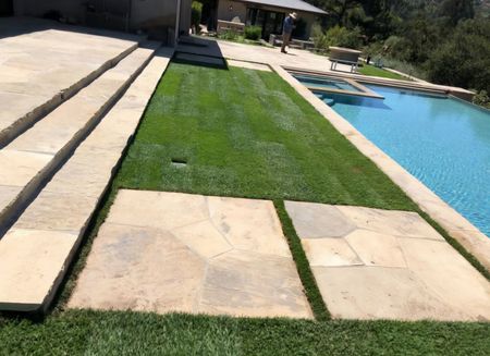 Person rolling out sod on a grassy lawn.