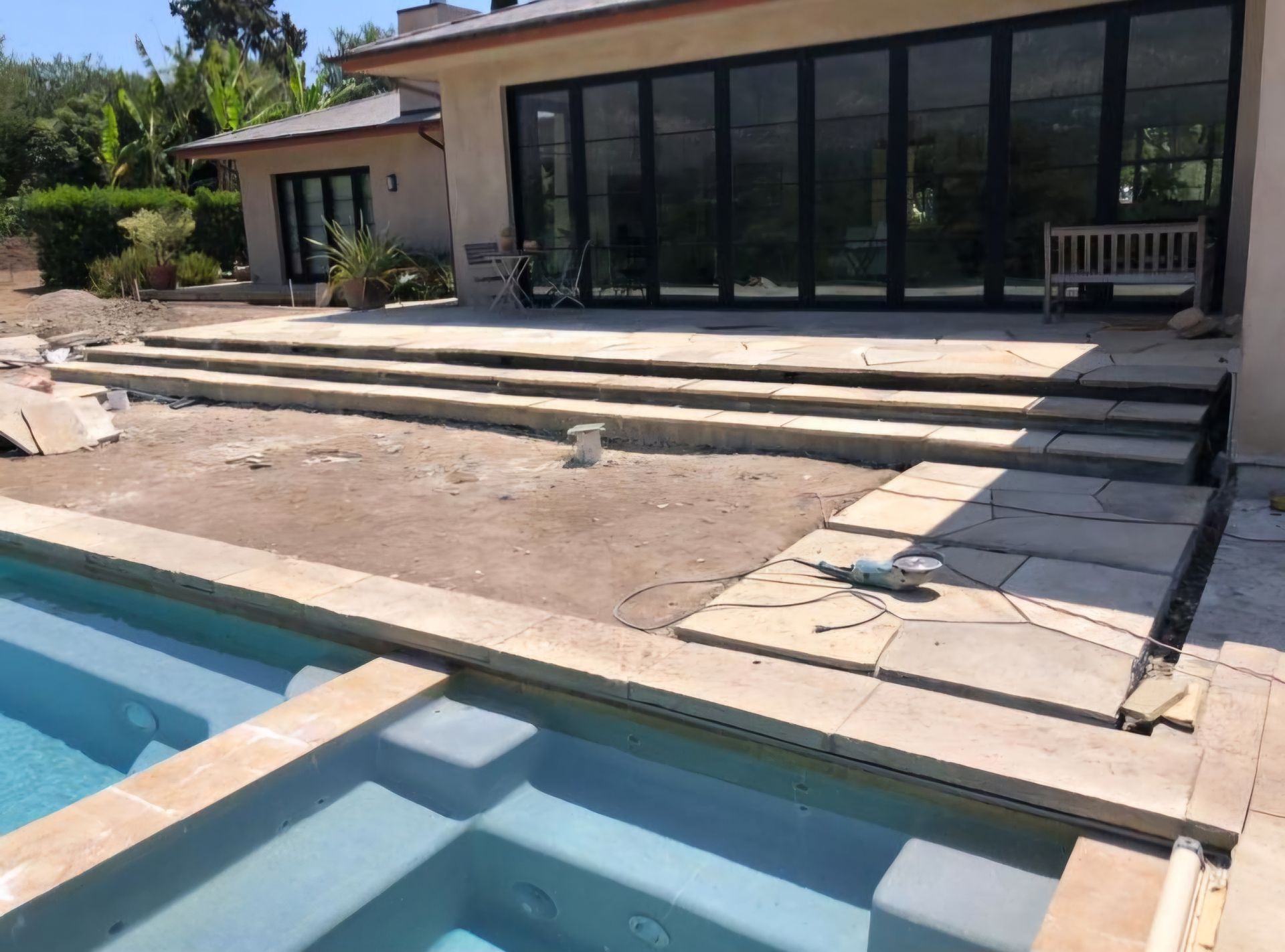 Pool and patio under construction with steps leading to house and folding glass doors.