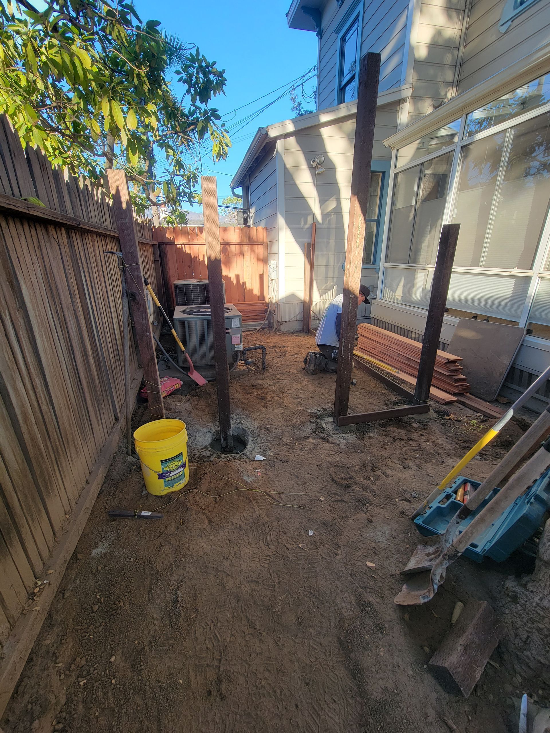 Construction site with wooden posts, a bucket, and tools in a backyard.