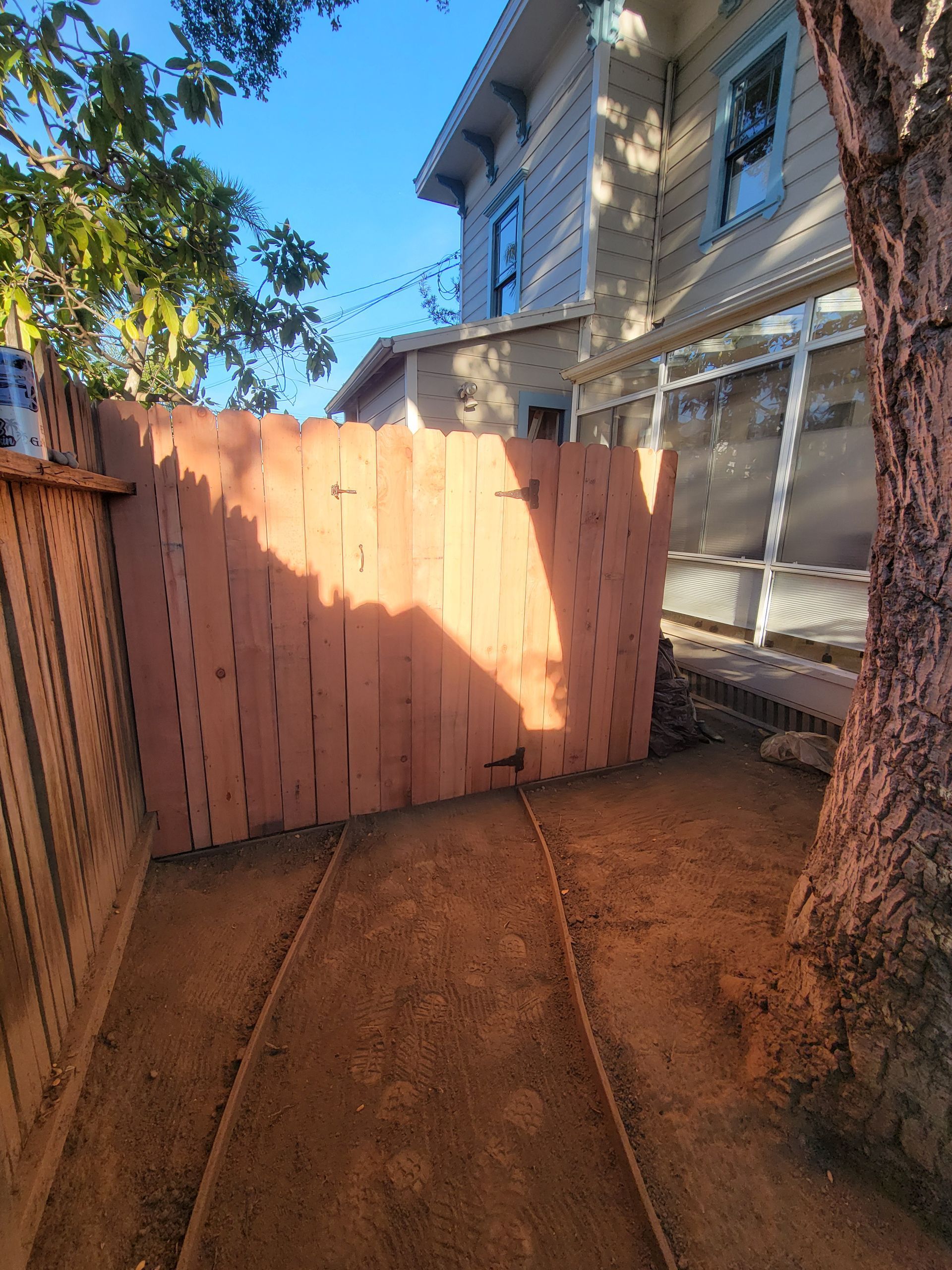 Wooden fence in a dirt yard, with a house in the background and a tree on the right.
