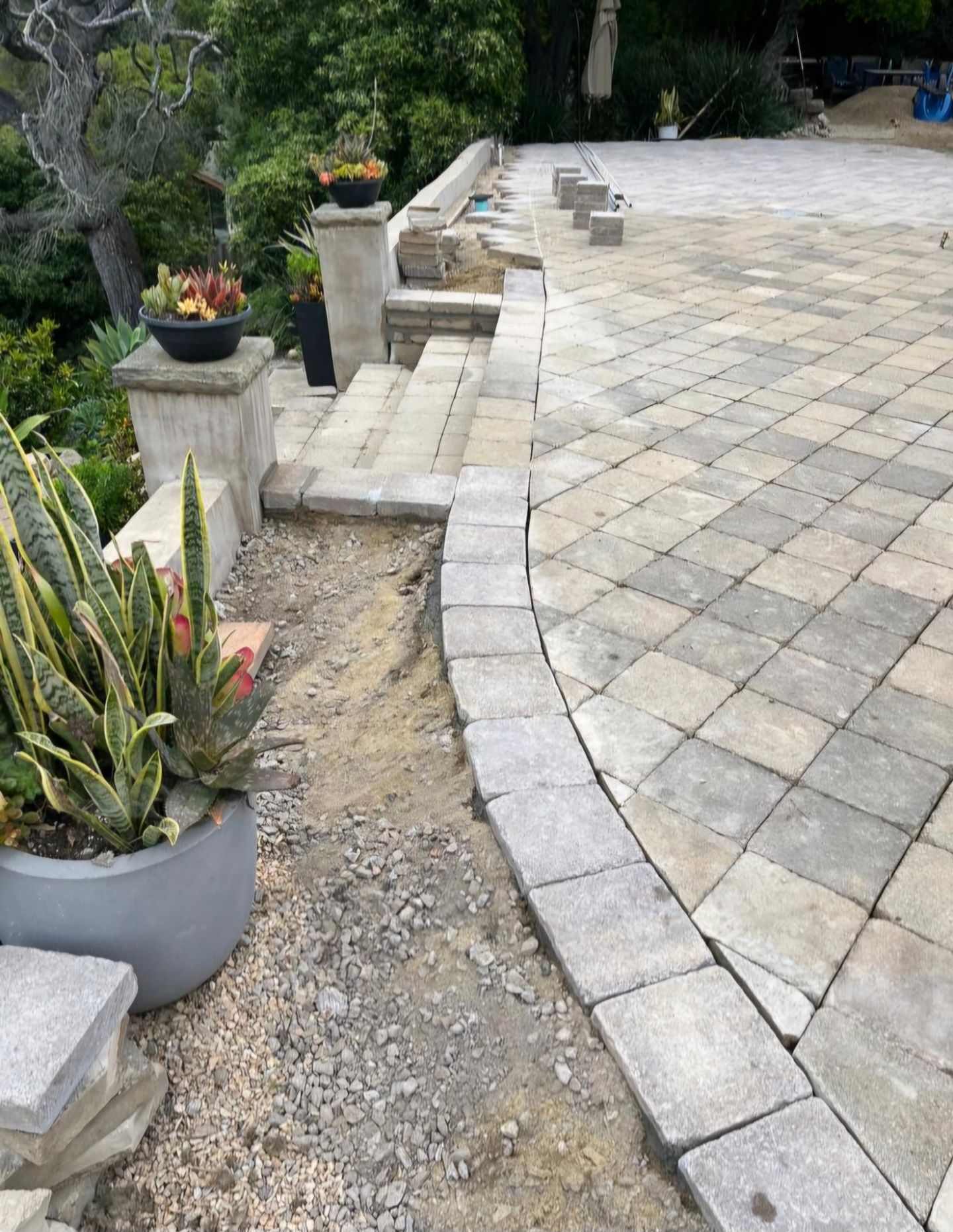 Patio with stone pavers and steps, next to a garden with potted succulents.