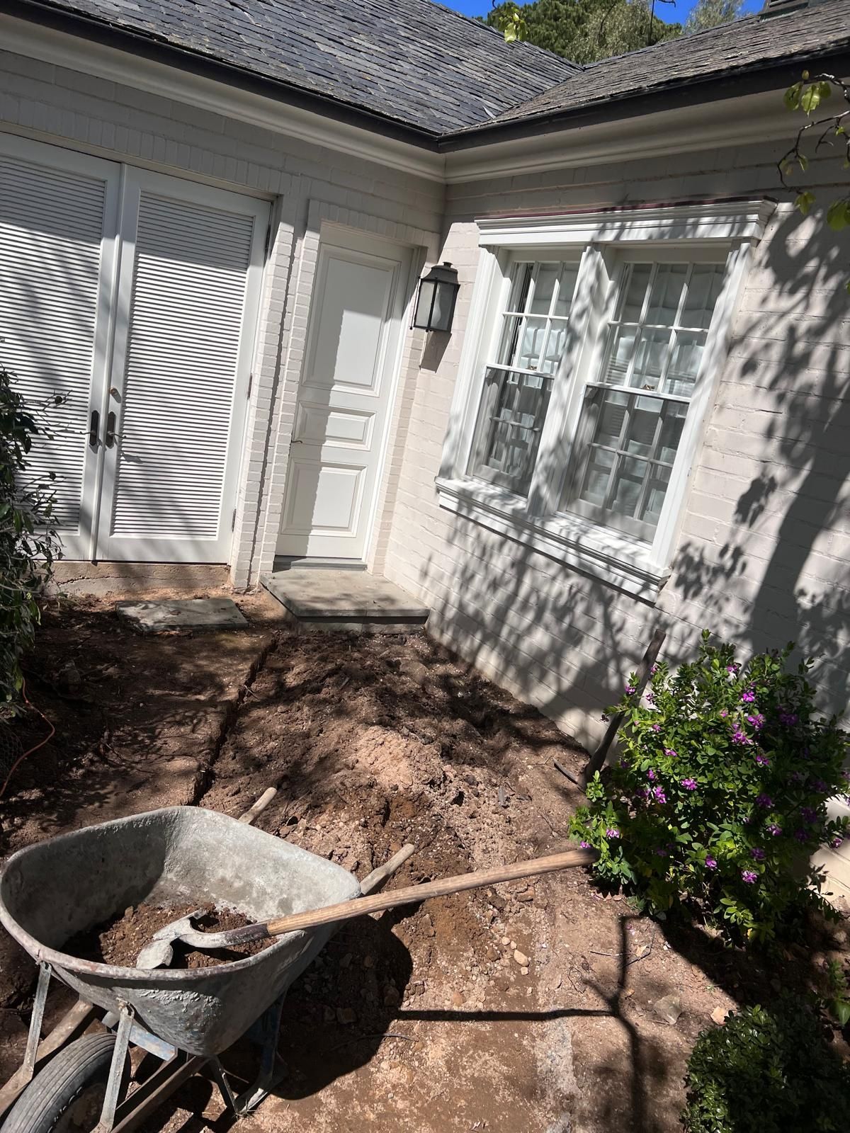 Wheelbarrow on dirt area near white building with door and window.
