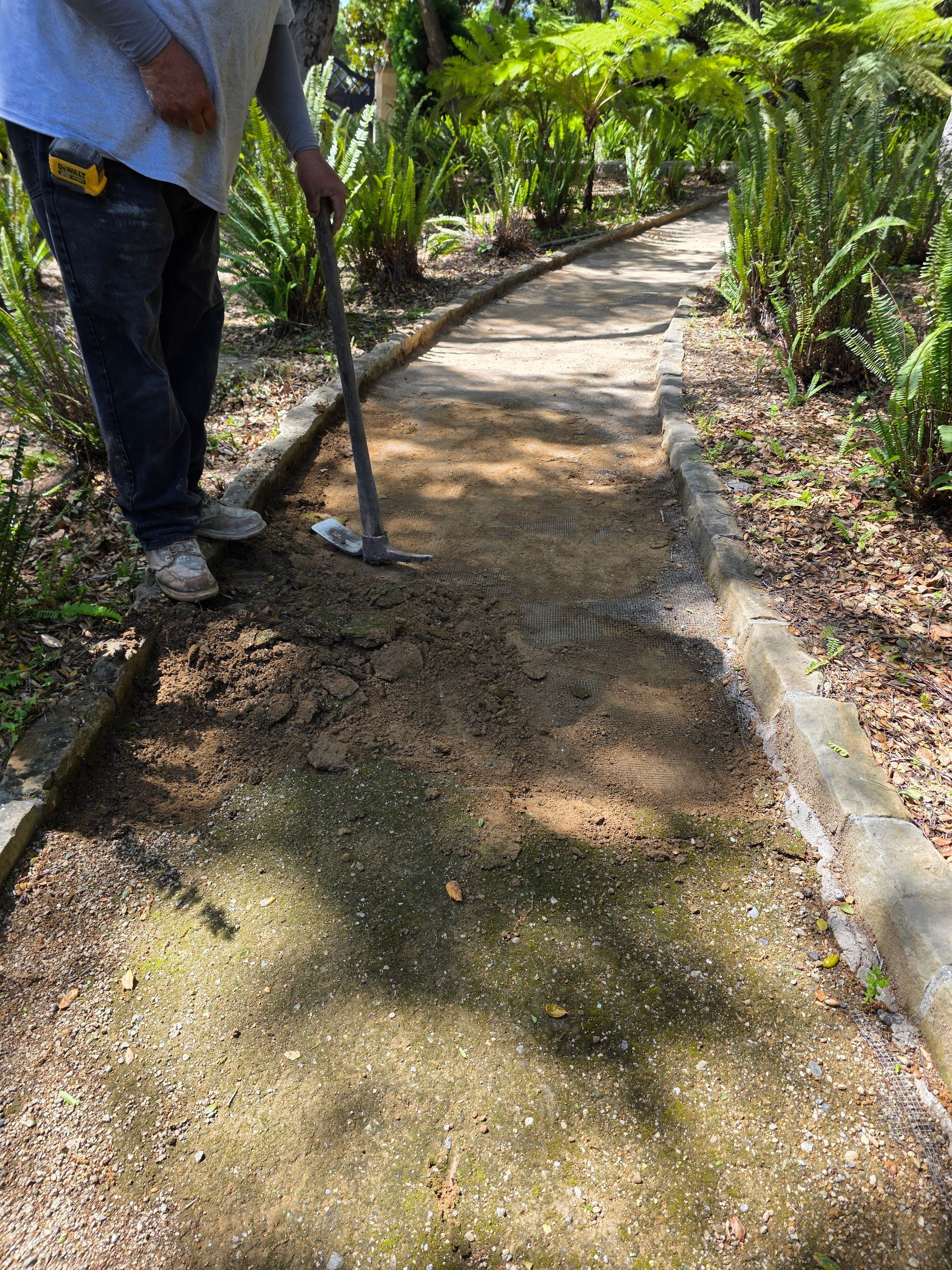 Person leveling gravel on a garden path with a tool.