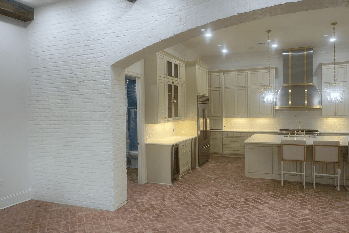 A light-filled kitchen after remodeling with white cabinetry, a brick wall, and a marble-look floor.