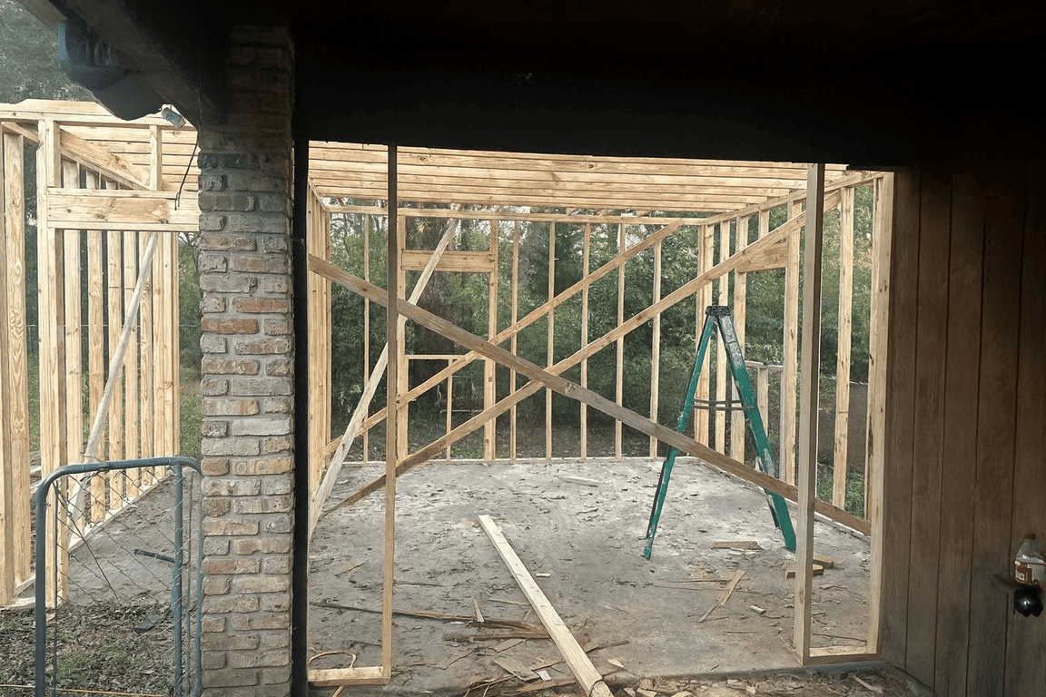 Wooden frame of a building under construction near Youngsville, with a brick wall on the left.