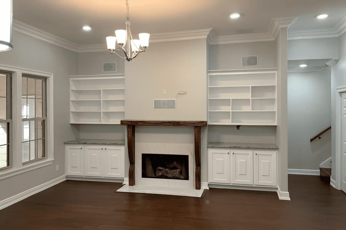 Living room remodel in Lafayette, LA, with a fireplace, built-in white shelves, dark wood floors, and a chandelier.