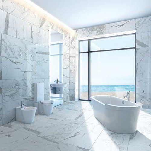 A bathroom with marble tiles , a bathtub , toilet , bidet and a large window.