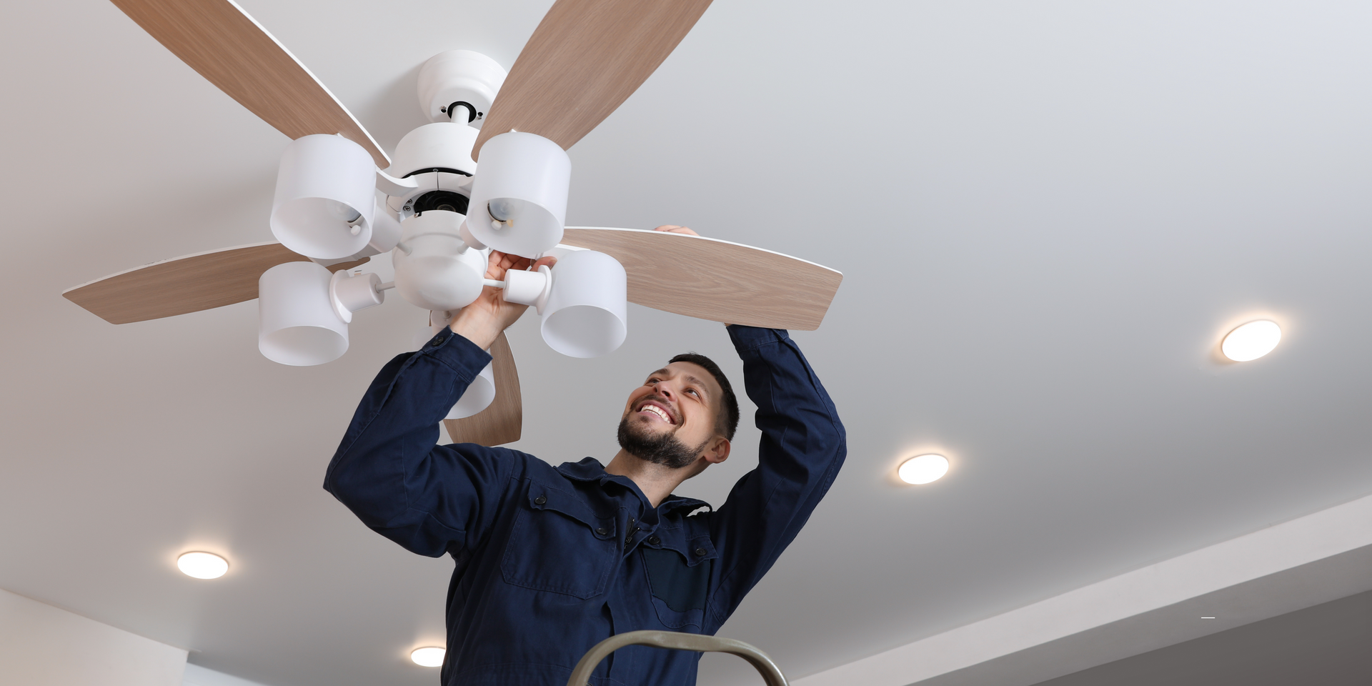 A man is fixing a ceiling fan in a living room.