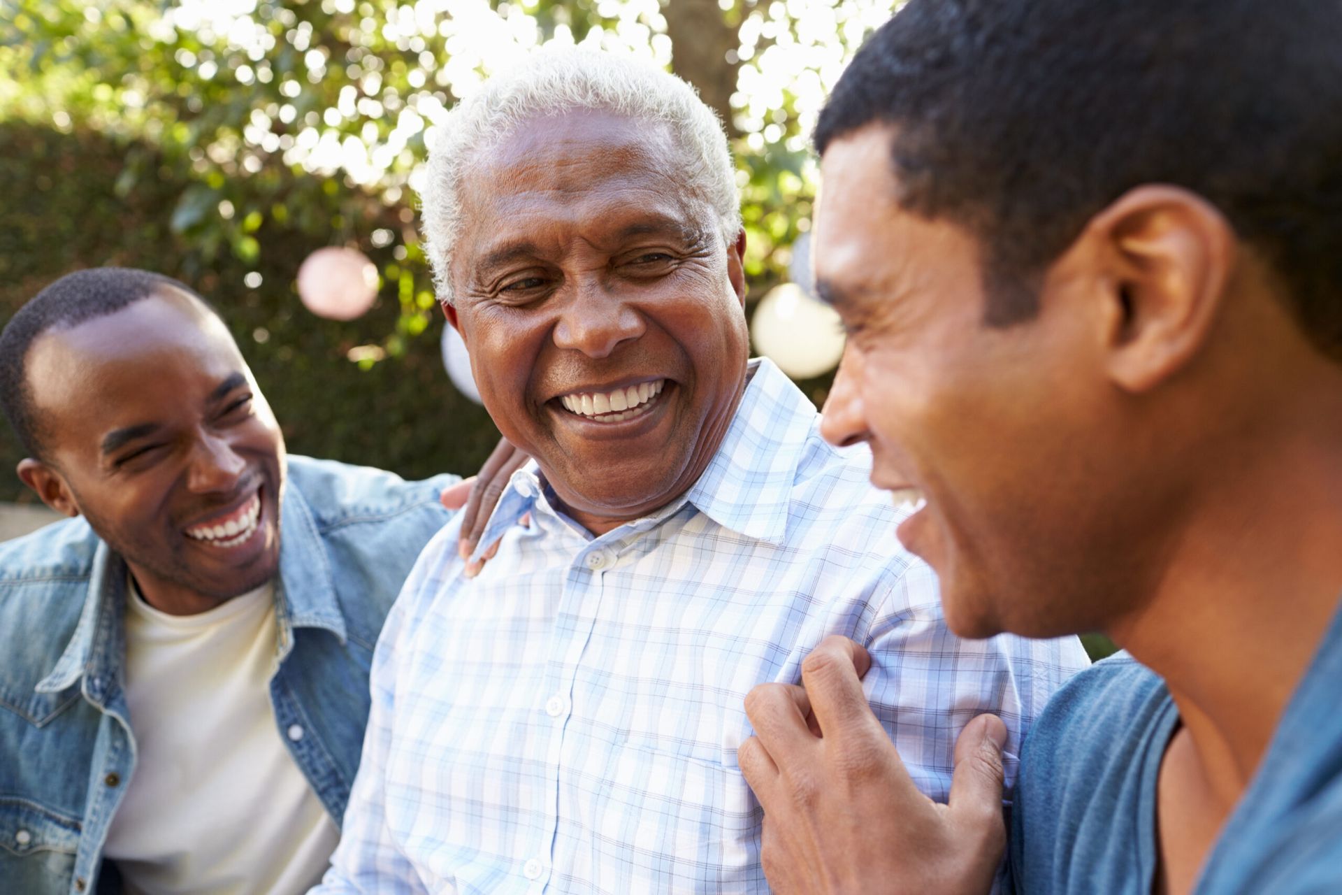 Three people smiling and laughing together outdoors in a sunny park.