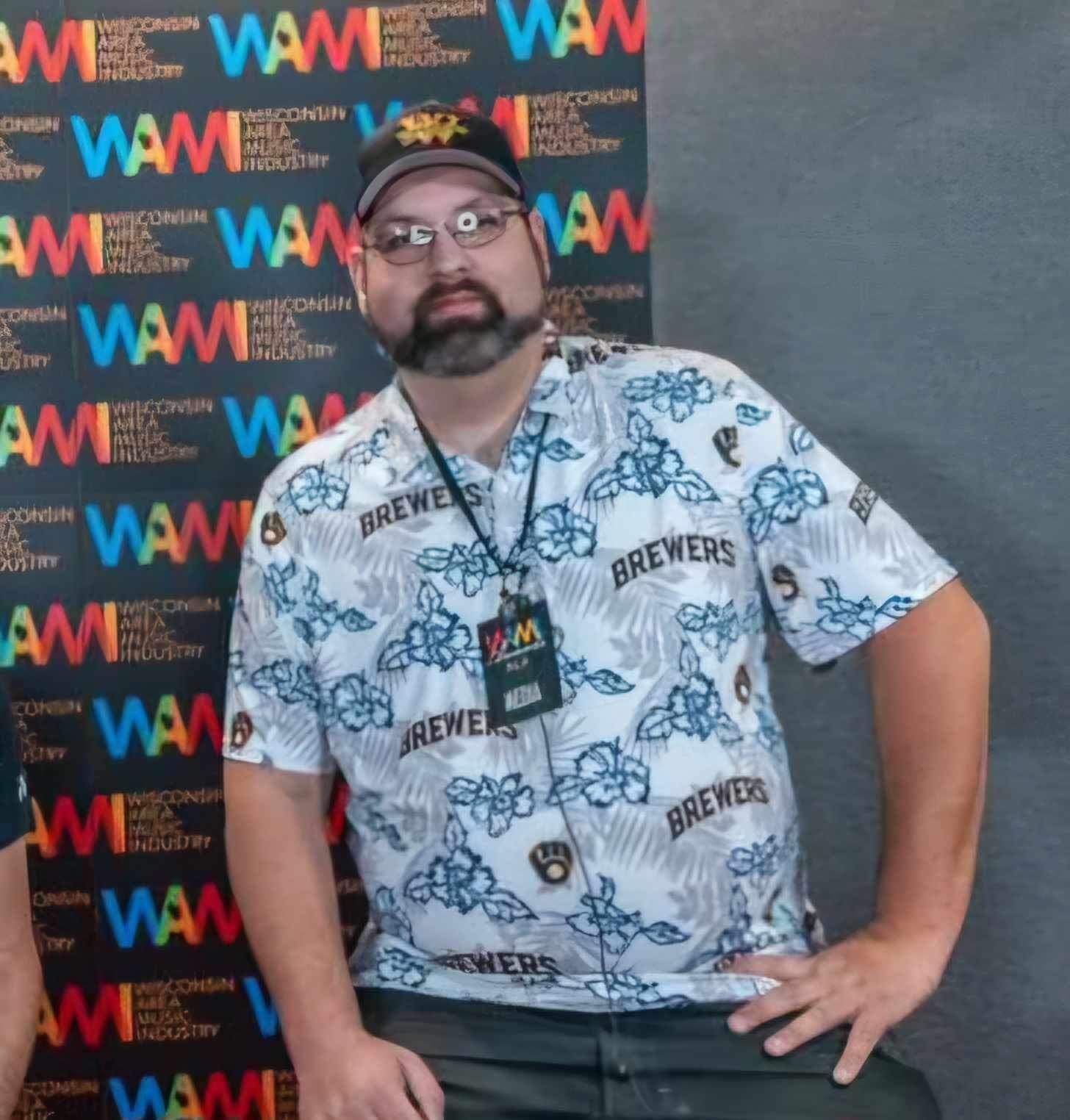 A man wearing a brewers shirt stands in front of a wall