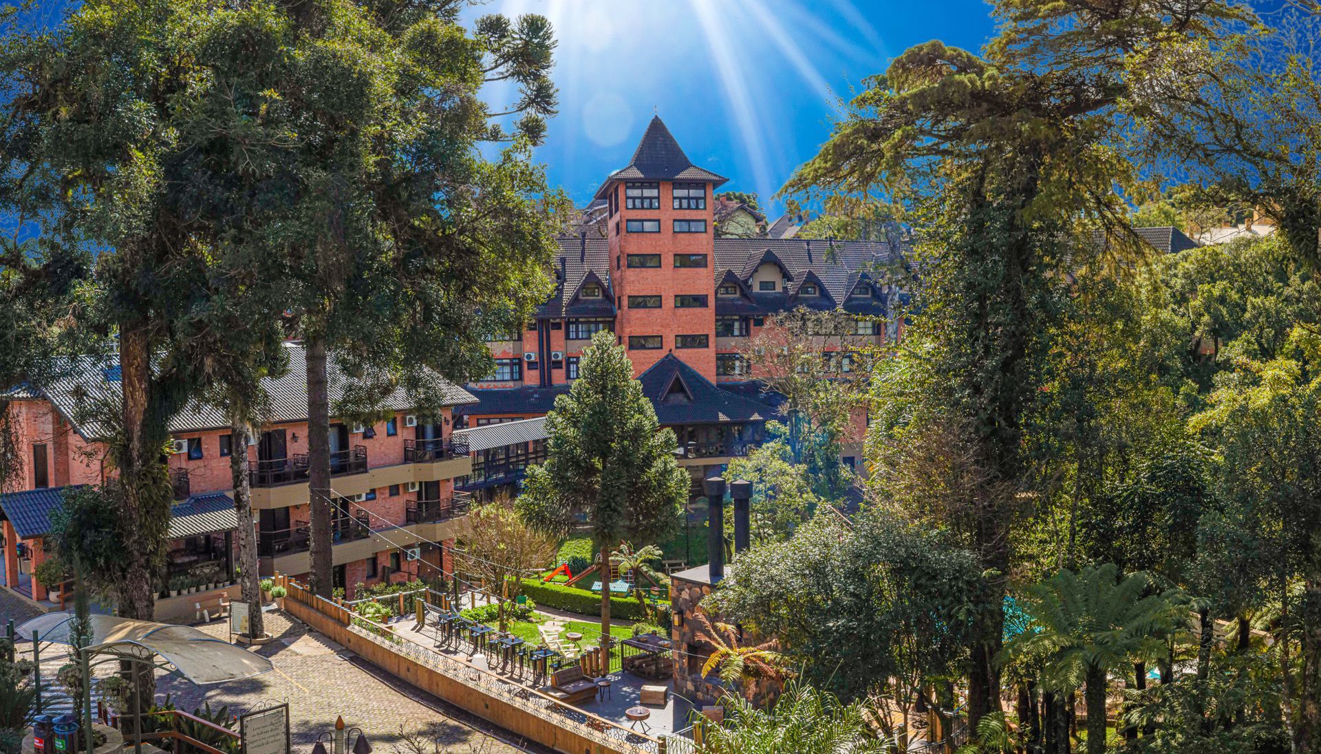 Hotel com piscina e espreguiçadeiras; rodeado por árvores.