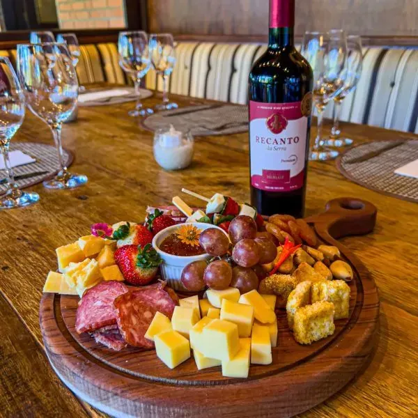 Tábua de charcutaria com vinho tinto, uvas, queijo, linguiça, morangos e biscoitos sobre uma mesa de madeira.