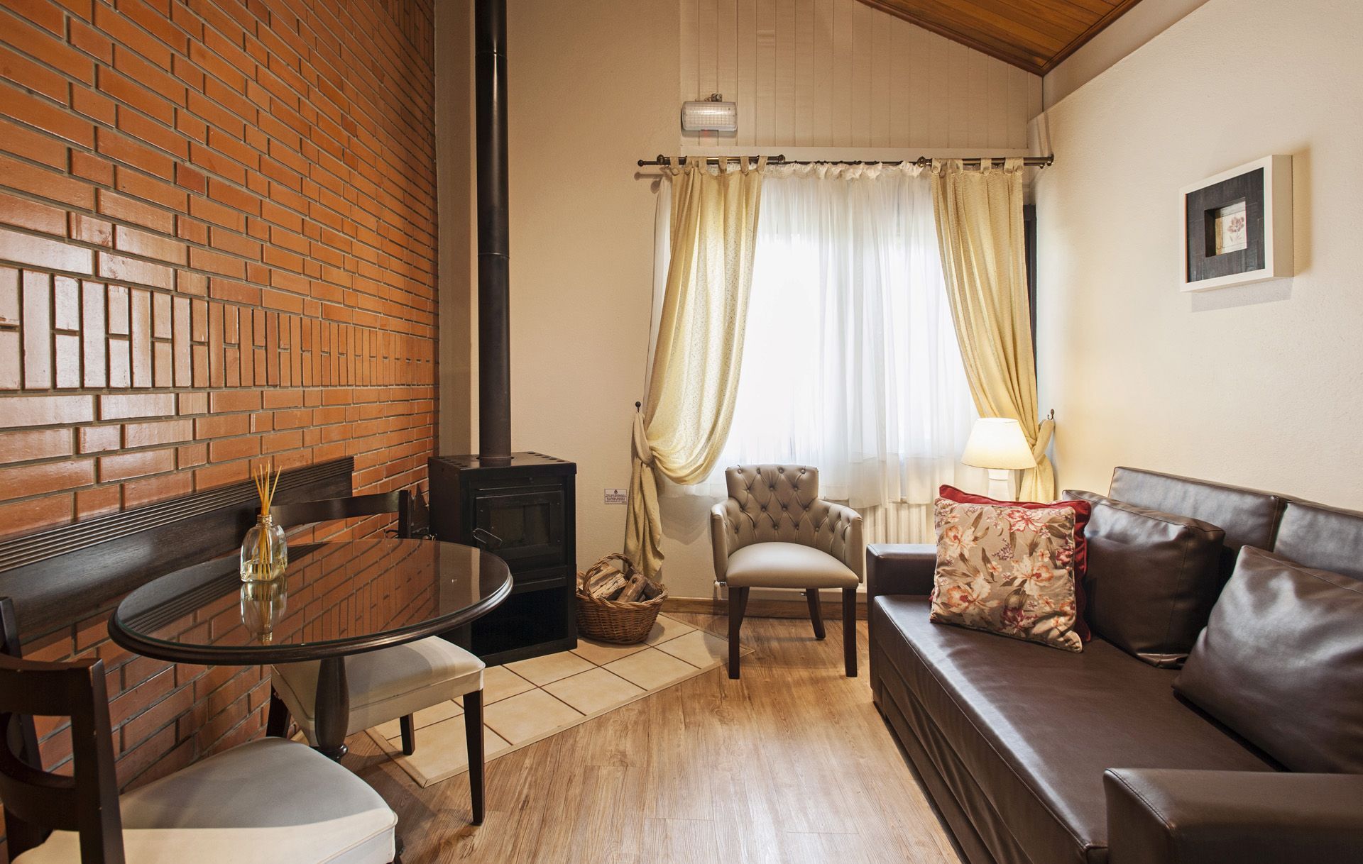 Quarto aconchegante com teto de madeira, área de estar, mesa redonda, sofá verde e mesa de jantar perto da janela.