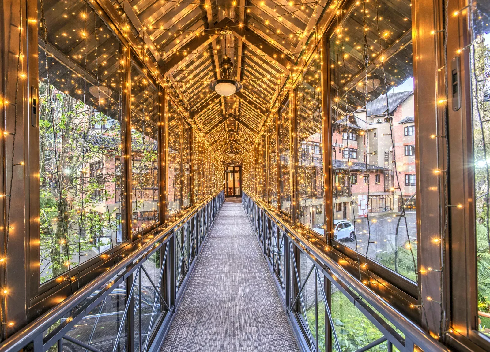 Ponte coberta iluminada por cordões de luzes quentes. Prédios residenciais ao fundo.