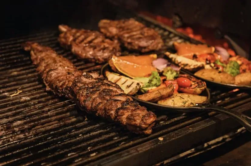 Bife grelhado com legumes, incluindo abóbora, batatas e tomates.