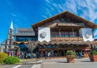 Um edifício em estilo bávaro com uma torre de igreja. Pessoas reunidas do lado de fora em um dia ensolarado.