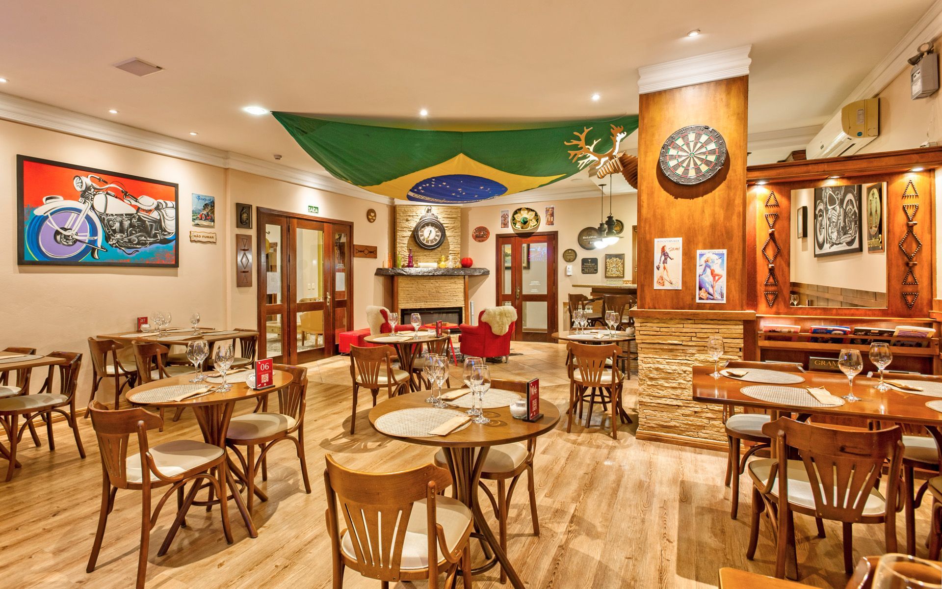 Interior de um restaurante decorado com uma bandeira brasileira, bar, mesas e poltronas vermelhas.