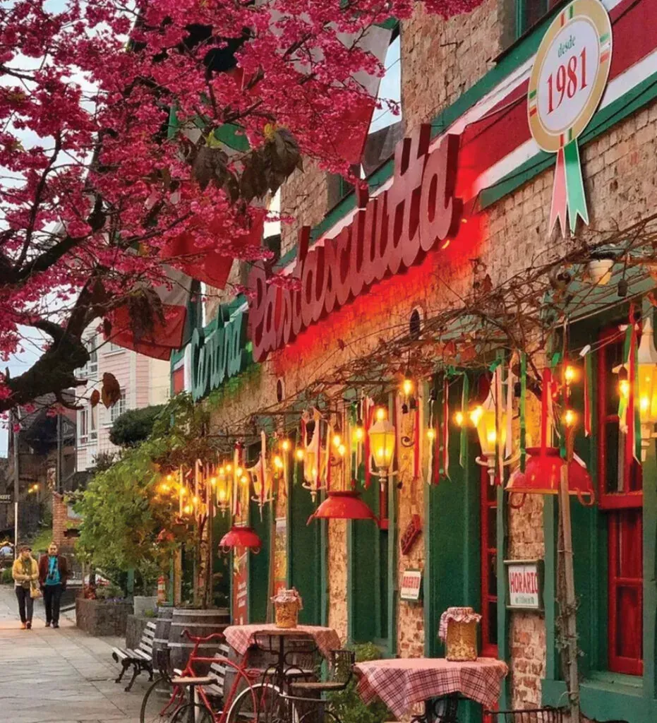 Fachada do restaurante com detalhes em vermelho e verde, lanternas e uma árvore rosa em flor.