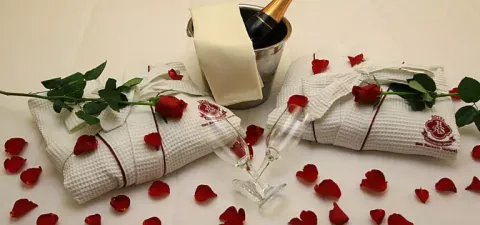 Ambiente romântico de hotel com champanhe, roupões de banho, pétalas de rosa e flores.