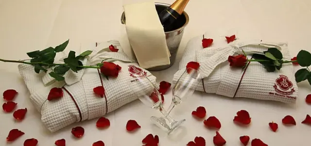 Ambiente romântico de hotel com champanhe, roupões de banho, pétalas de rosa e flores.
