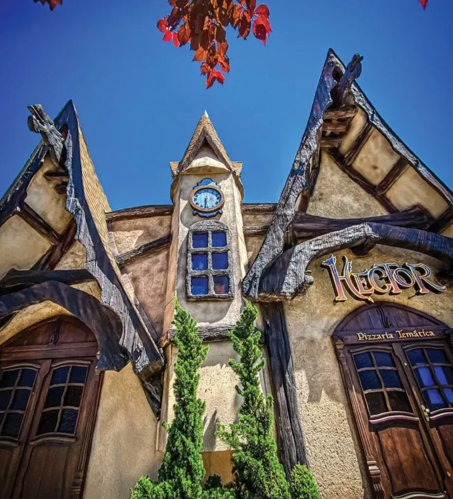 Prédio pitoresco com torre do relógio e placa "Igor", sob um céu azul brilhante. Portas e estrutura de madeira em tons de marrom, árvores verdes.