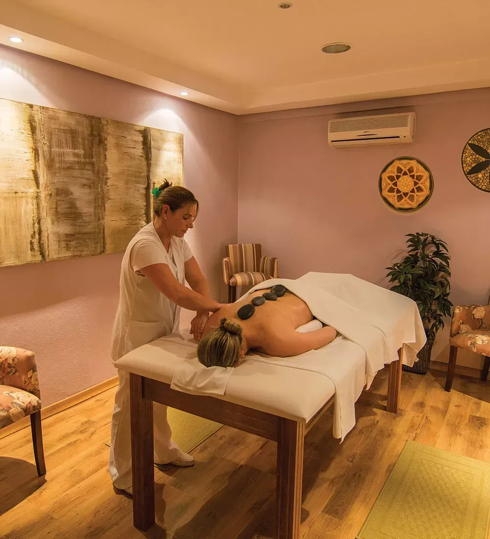 Massagista aplicando massagem com pedras quentes em uma sala de spa.