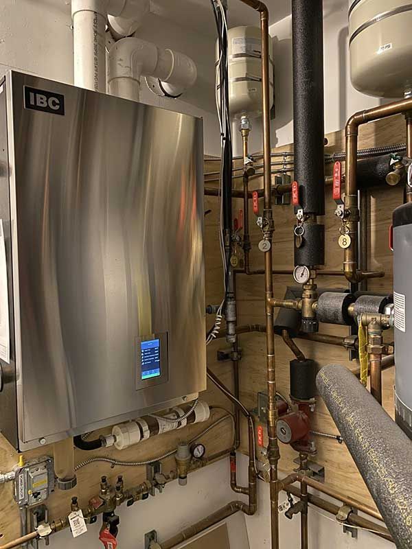 Stainless steel IBC boiler with copper pipes and valves in a utility room.