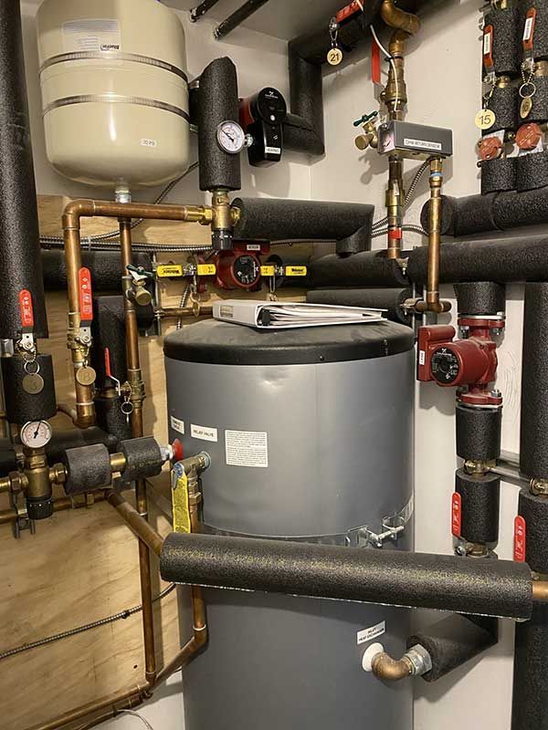 A water heater system with pipes, pumps, and a tank. Dark insulation, copper pipes, and red valves are visible.