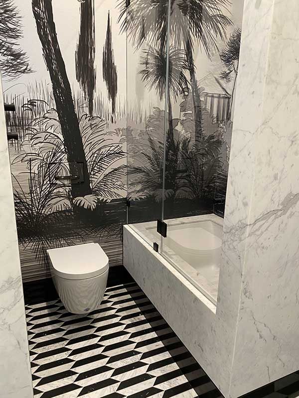 Bathroom with black and white wallpaper, patterned floor, toilet, and a bathtub with a glass partition.