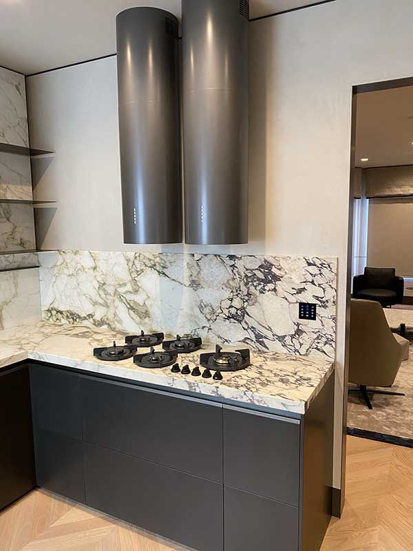 Modern kitchen with marble backsplash, dark gray cabinets, and stainless steel range hood.