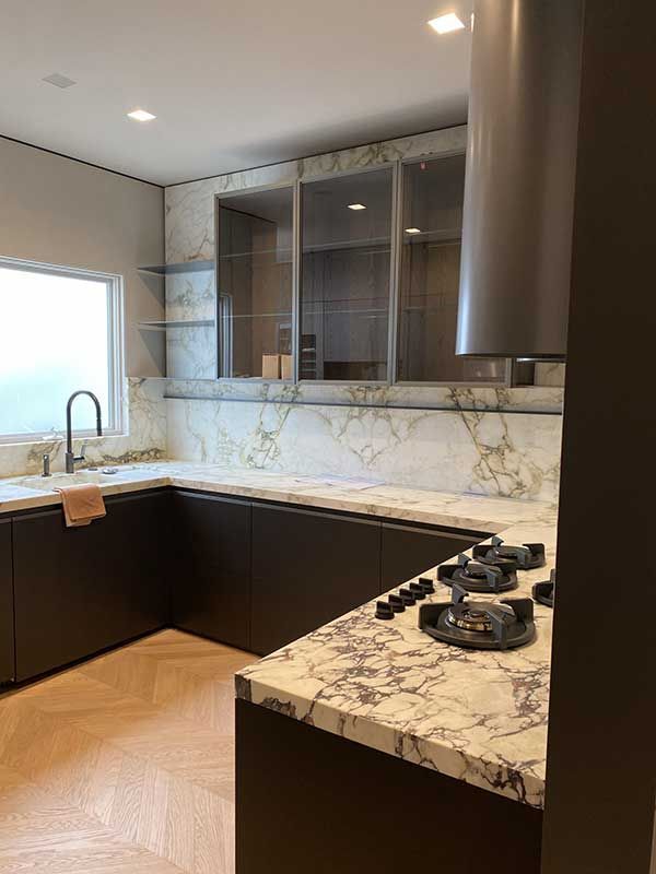 Modern kitchen with brown cabinets, marble countertops, stainless steel hood, and glass upper cabinets.