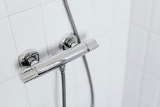 Silver shower faucet against white tiled wall.