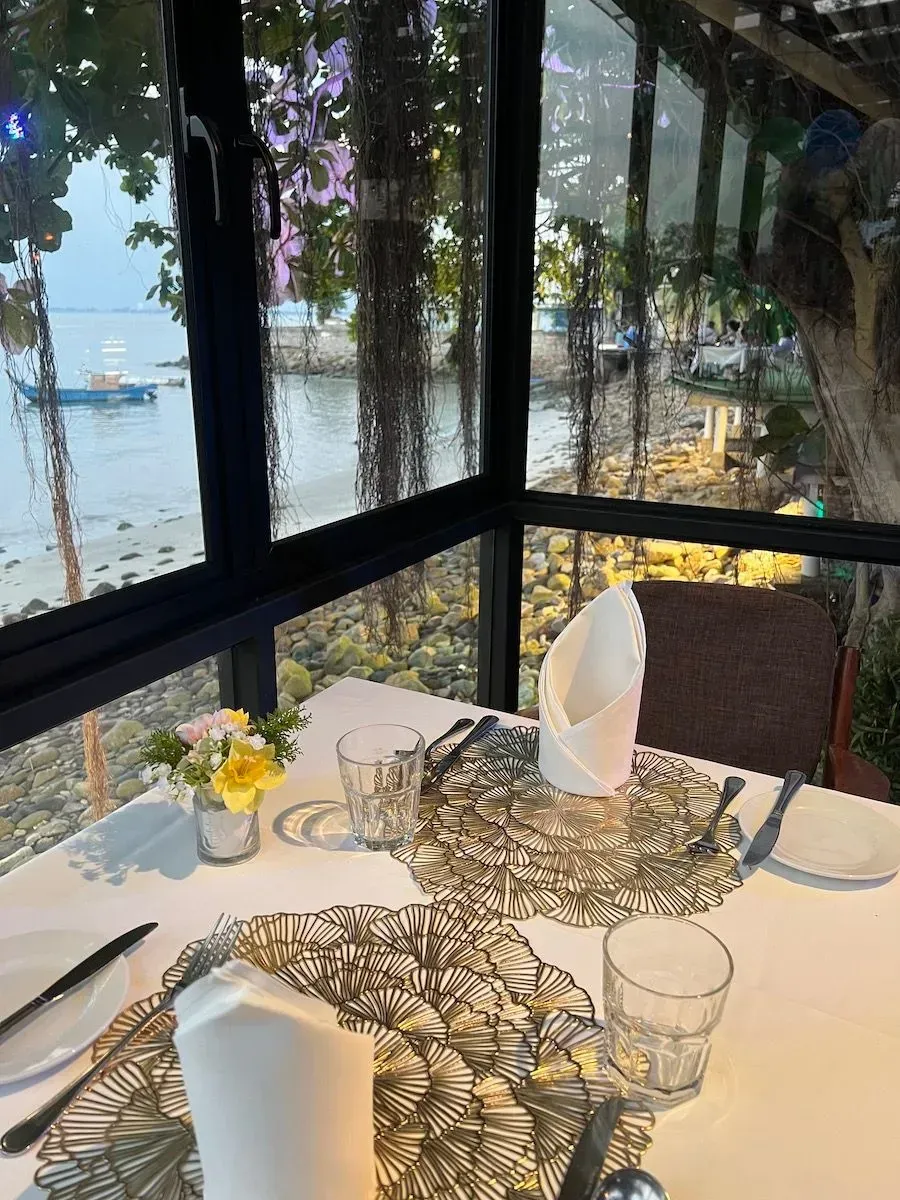 Restaurant table set for two, next to a window with a water view.