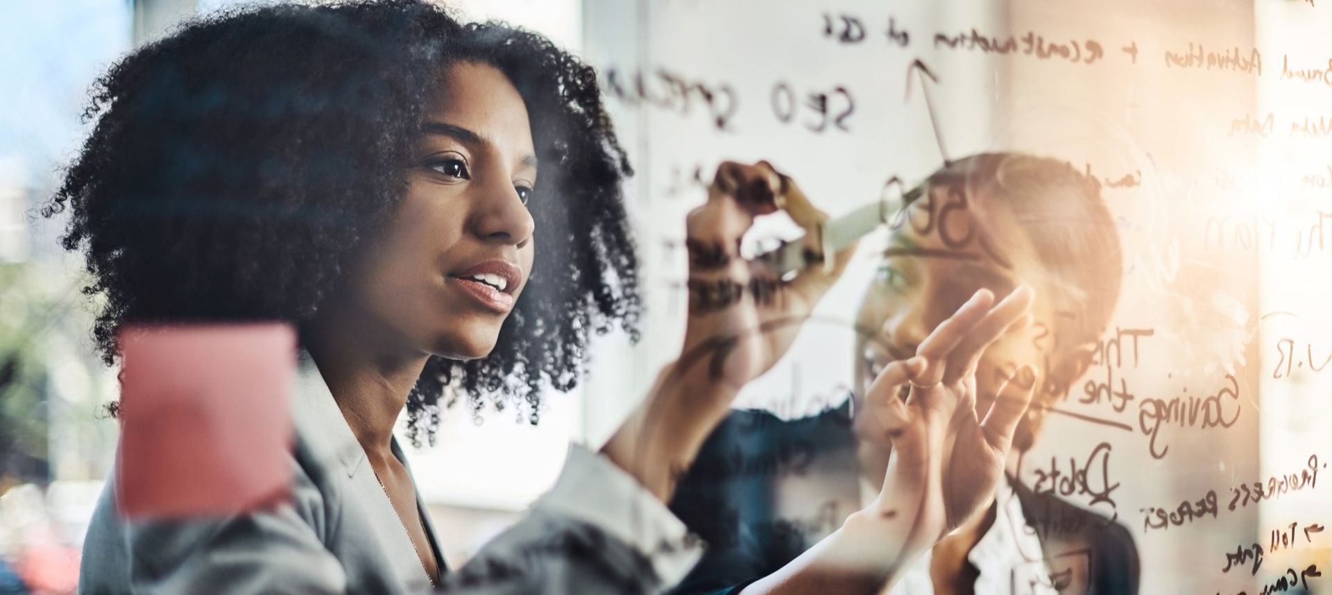 Three people in business attire at a table with laptop, smiling and talking in a modern room.