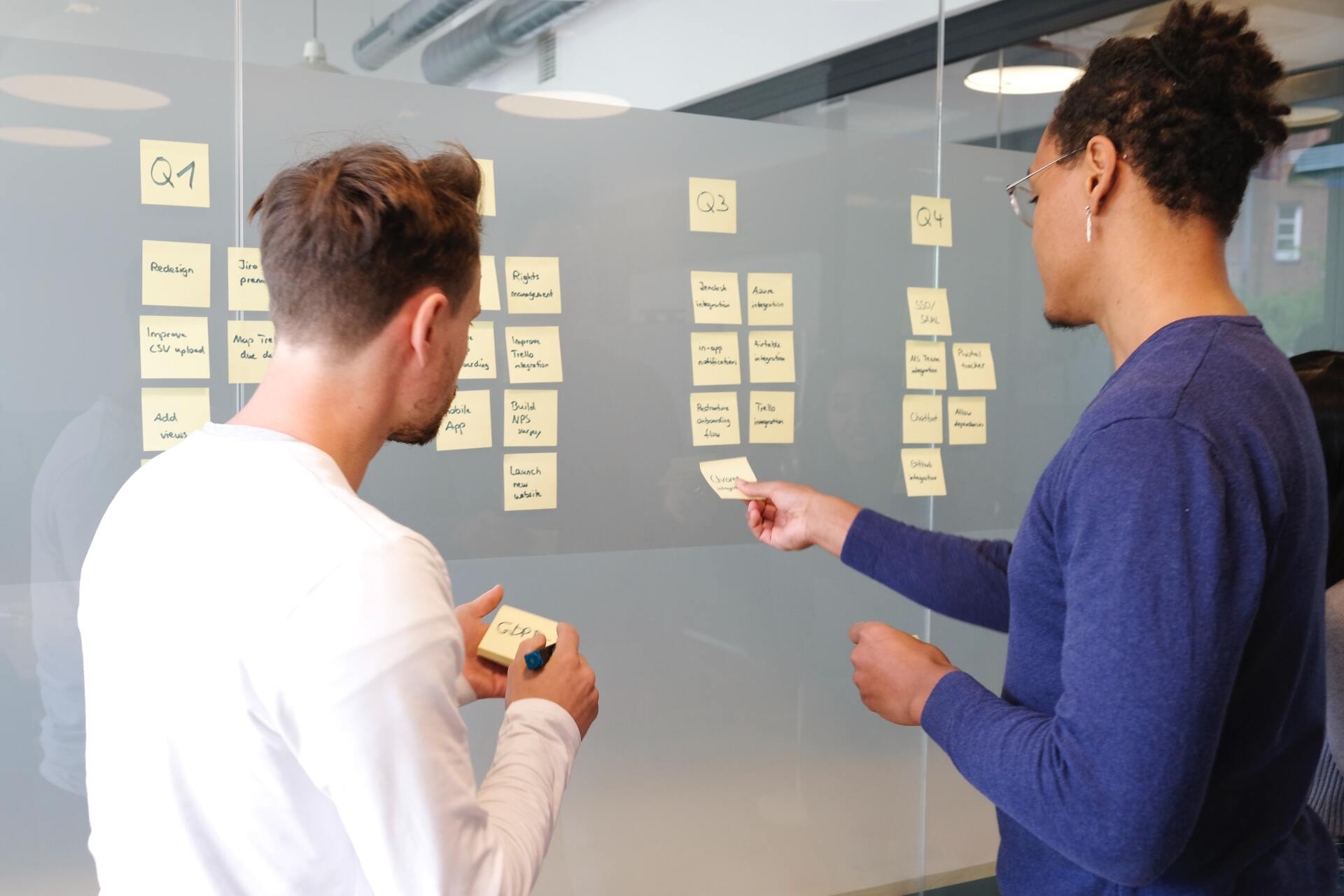 two men are looking at sticky notes on a glass wall .