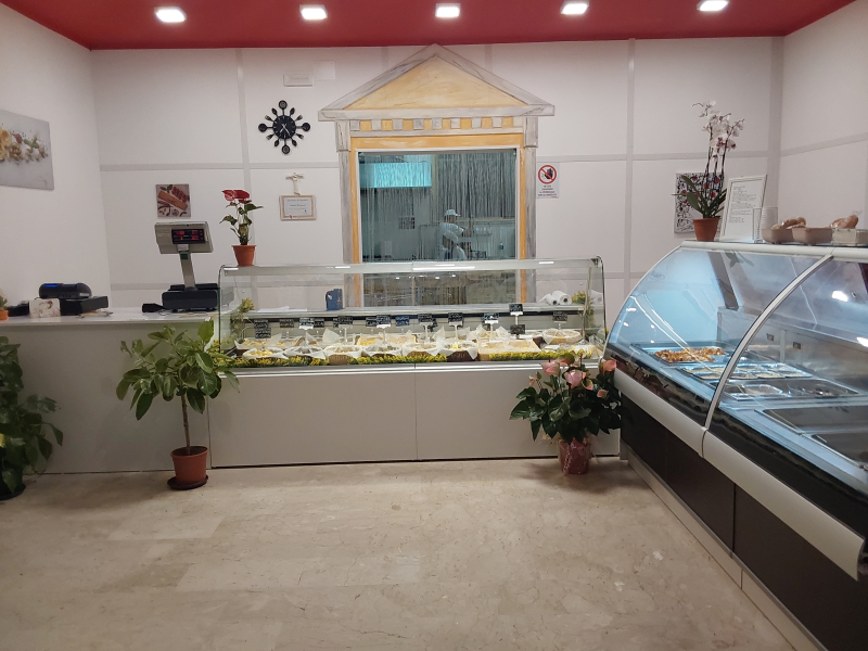 Interno di una gelateria con vetrine, registratore di cassa e decorazioni murali.