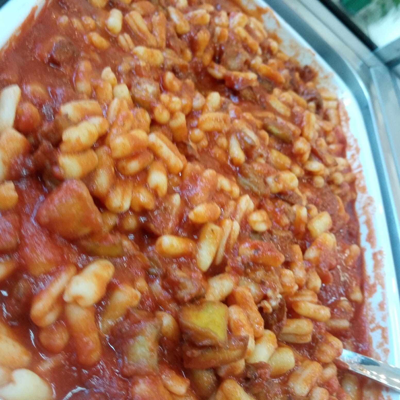 Fagioli bianchi e pasta in salsa di pomodoro rosso, serviti in un piatto bianco.