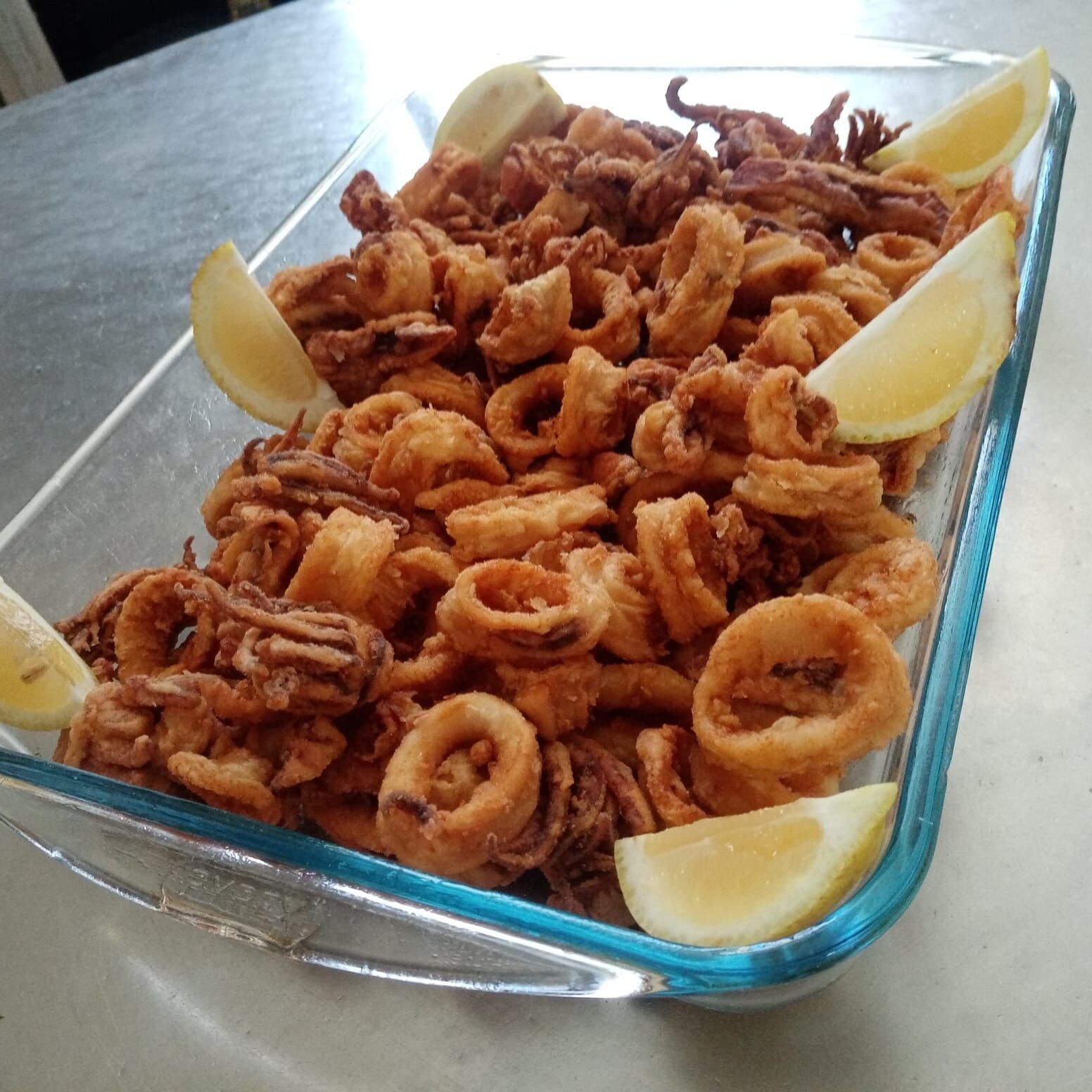 Calamari fritti in una pirofila di vetro, guarniti con spicchi di limone.