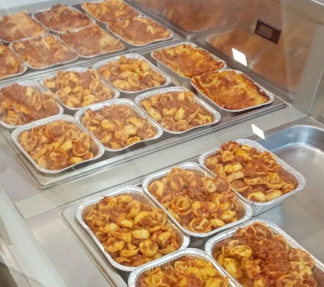 Piatti di pasta preparati in vassoi di alluminio, esposti in un banco gastronomia refrigerato.