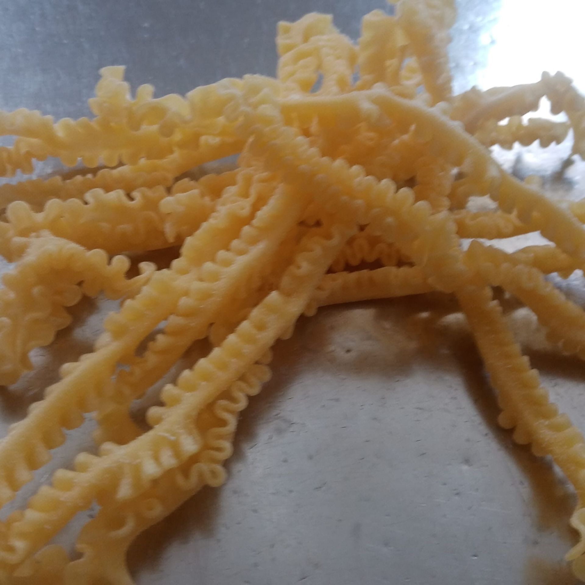 Mucchio di sottili, dorati e striati snack fritti su una superficie argentata.