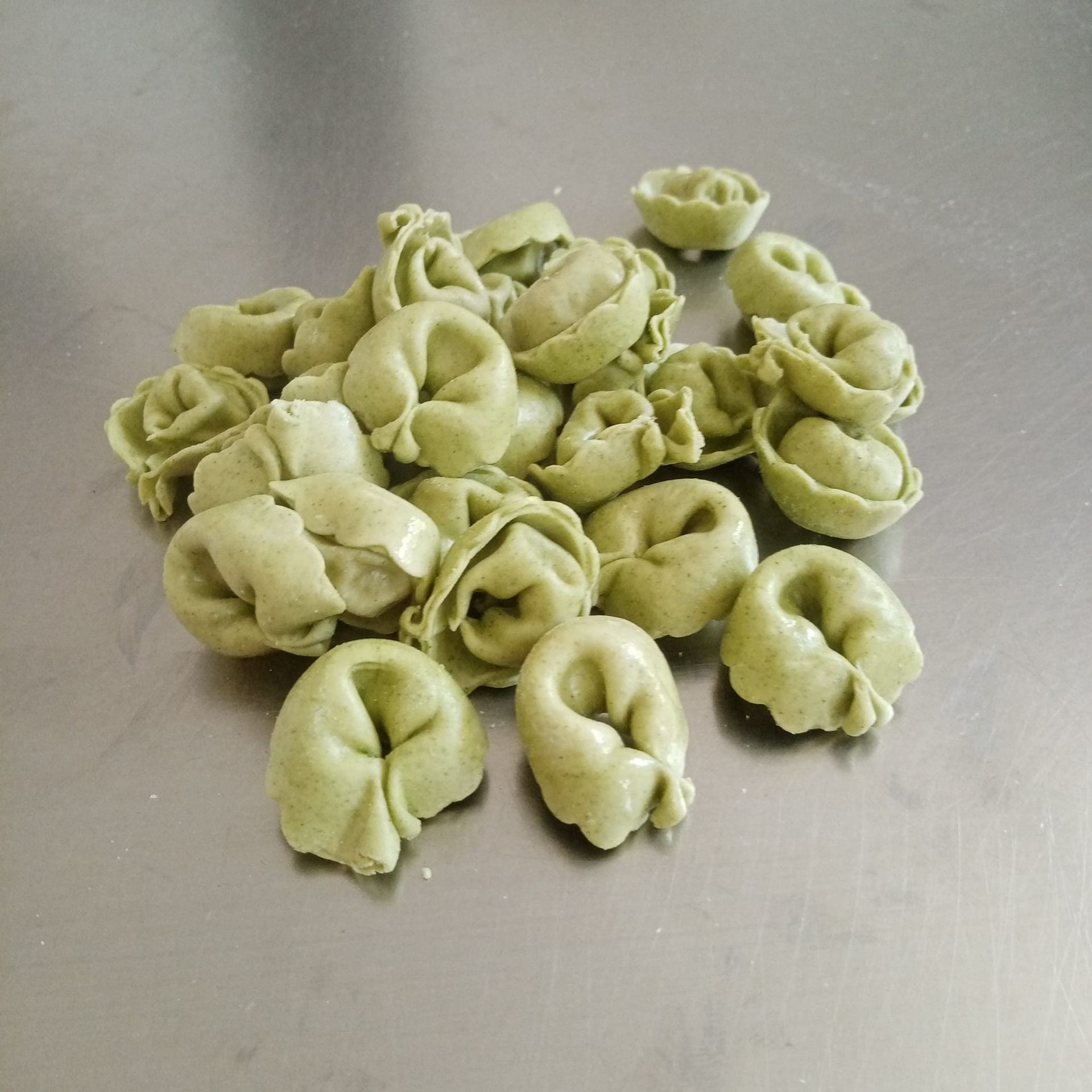 Pasta tortellini verde su una superficie in acciaio inox.