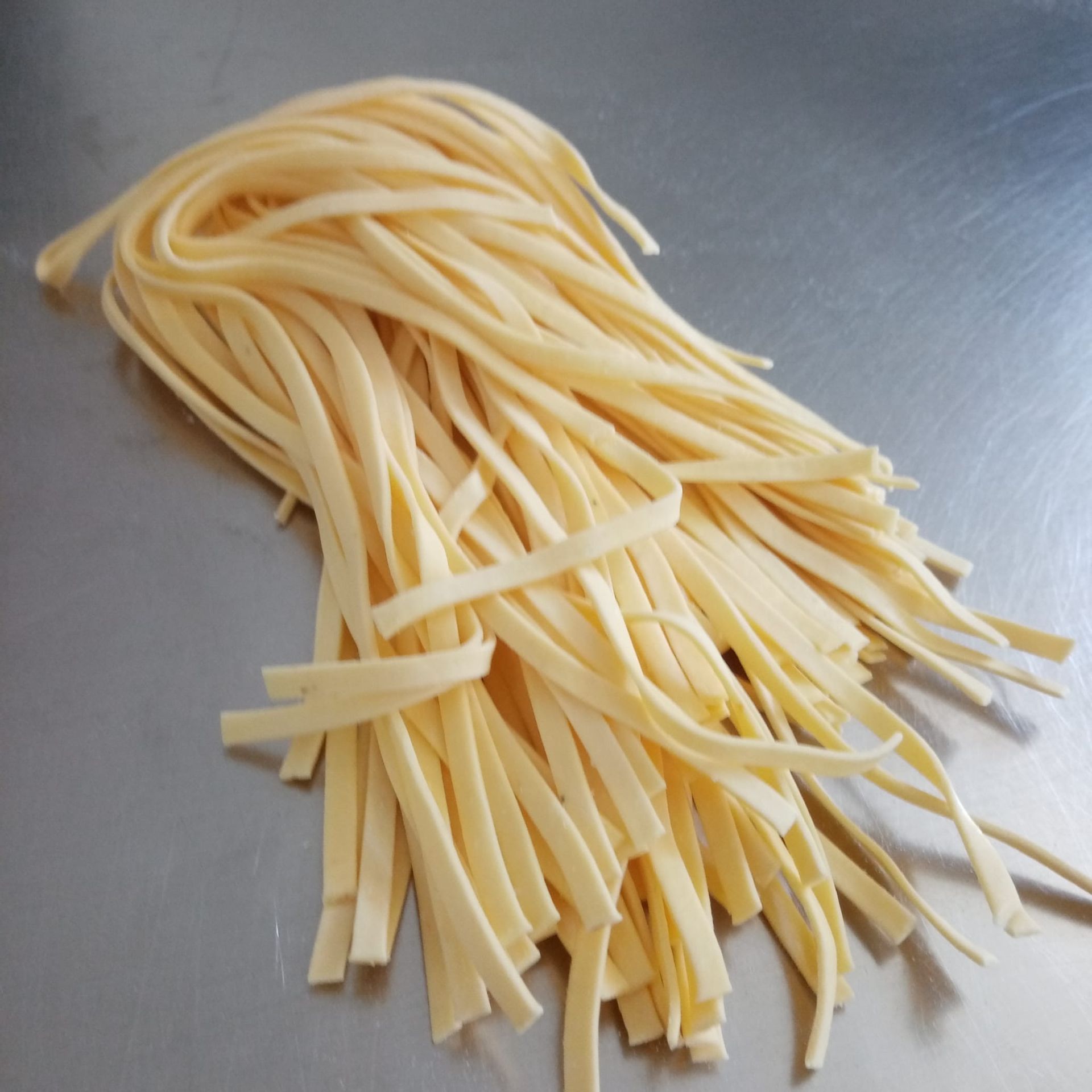 Fettuccine fresche e crude su una superficie in acciaio inossidabile.